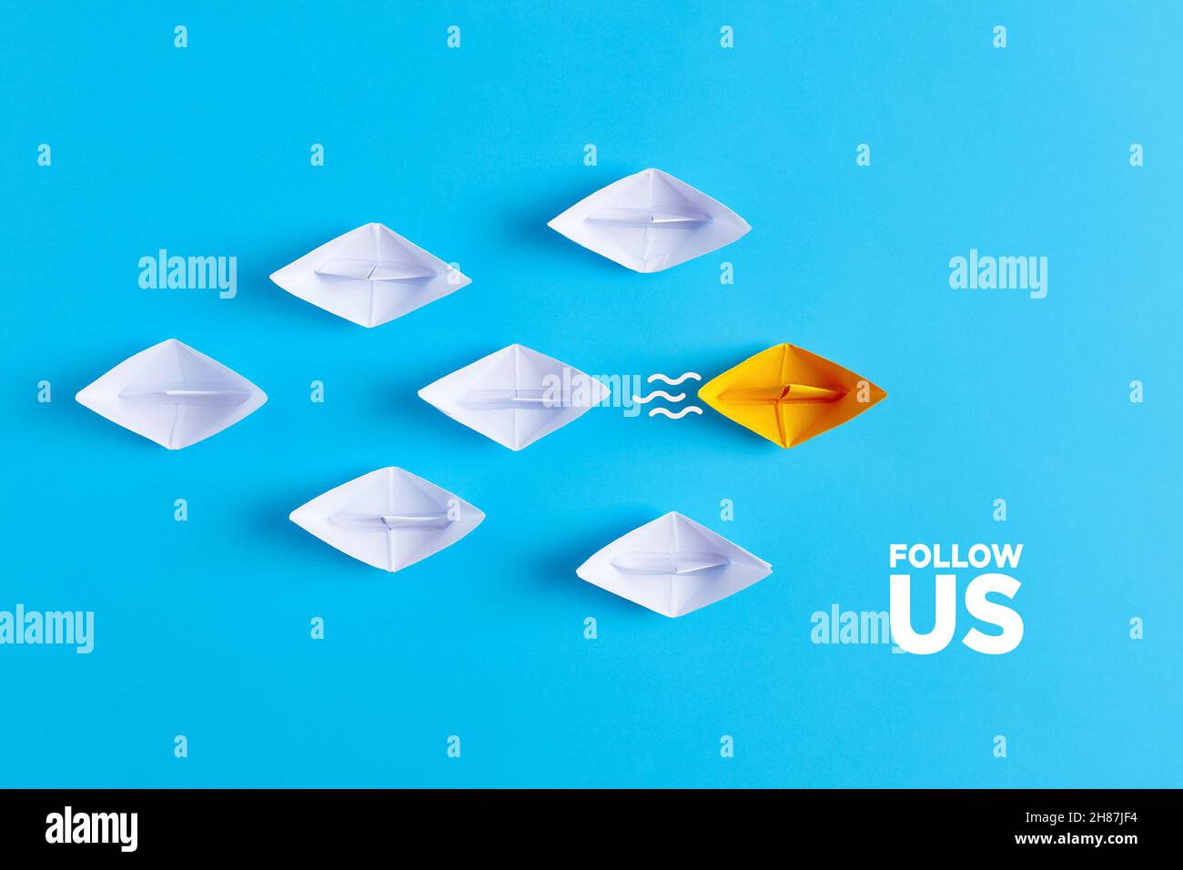 Gelbes Papierboot führt weiße Papierschiffe mit der Follow US-Nachricht. Social-Media- oder Internet-Follower-Konzept. Stockfoto