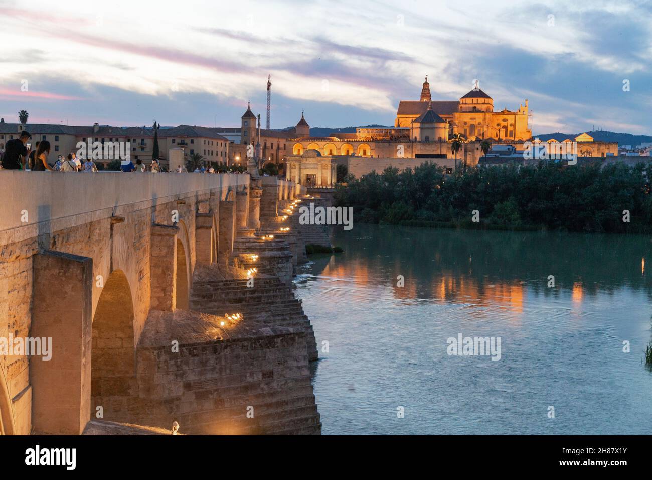 Blick auf die römische Brücke von Cordoba und die Moschee im Hintergrund mit Menschen, die in der blauen Stunde des Tages spazieren gehen Stockfoto