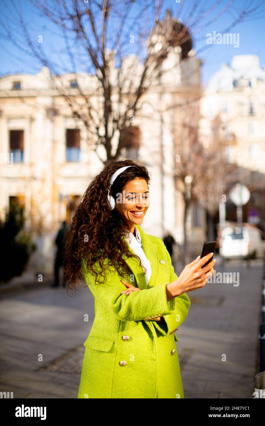 Hübsche junge Frau, die auf der Straße mit dem Smartphone Musik hört Stockfoto