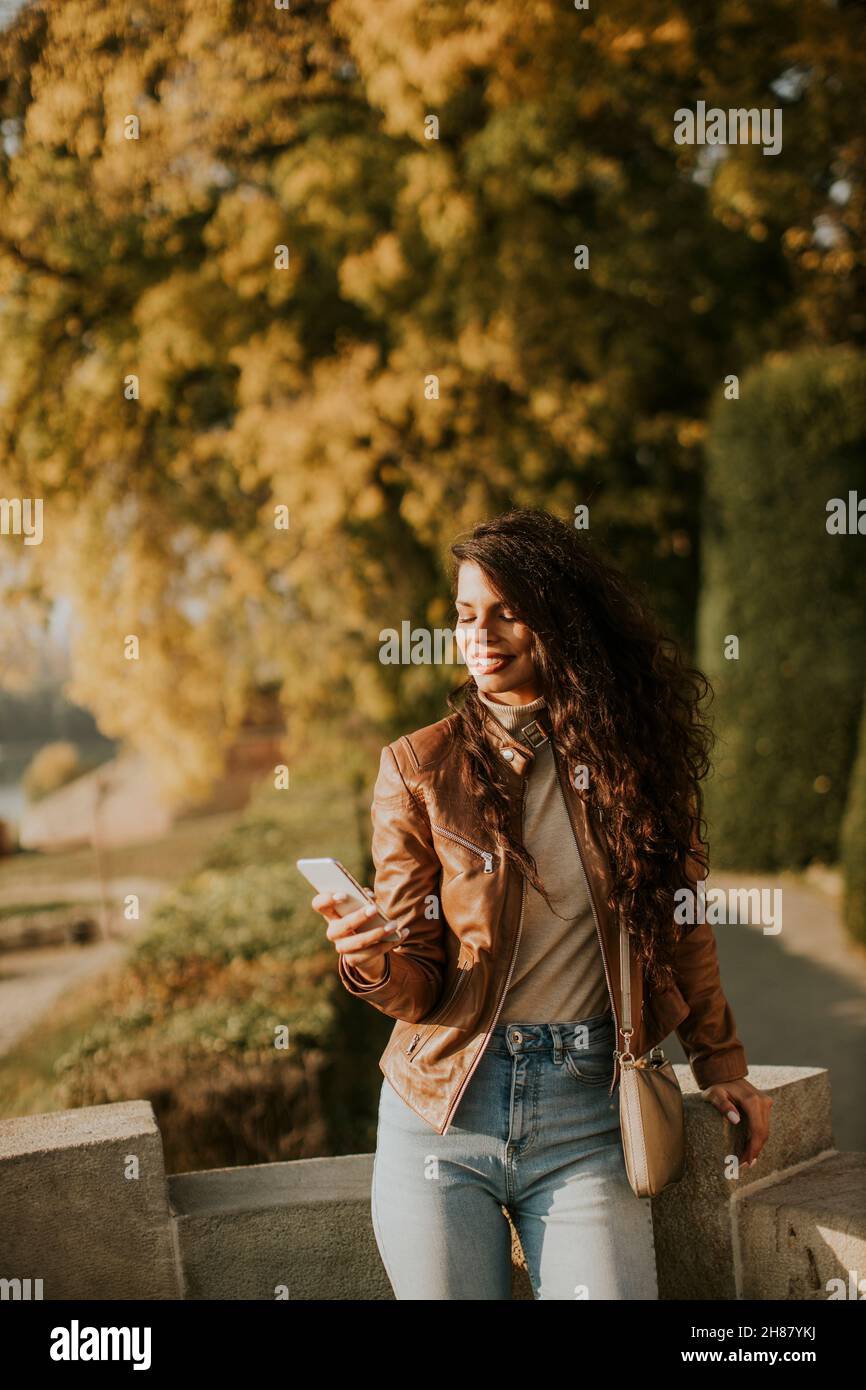 Hübsche junge Frau mit Handy im Park am sonnigen Herbsttag Stockfoto