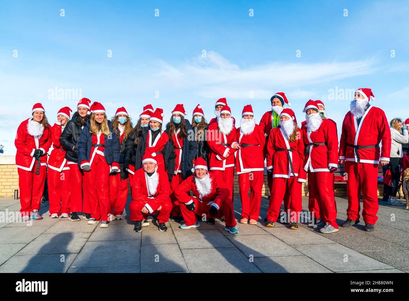 Eine Gruppe von Studenten des Kent College posiert für ein Gruppenbild, bevor sie an einem bitterkalten Morgen Ende November am karitativen Lauf „Santa's on the Bay“ teilnehmen, der den Pilgrims Hospices an der Strandpromenade von Herne Bay in Kent zu Hilfe geht. Stockfoto