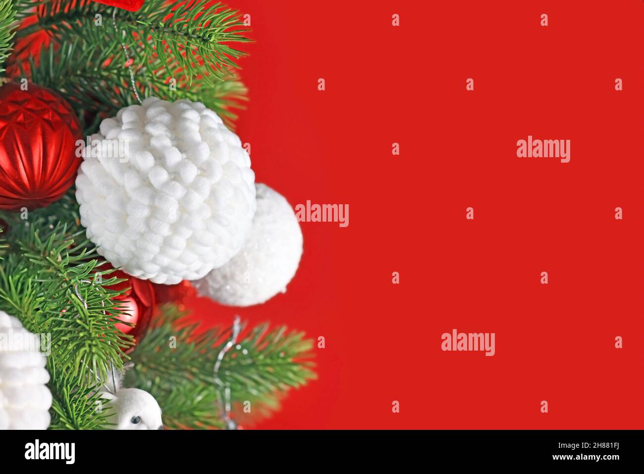 Flauschige weiße Weihnachtskugel auf geschmücktem Baum mit rotem Hintergrund Stockfoto