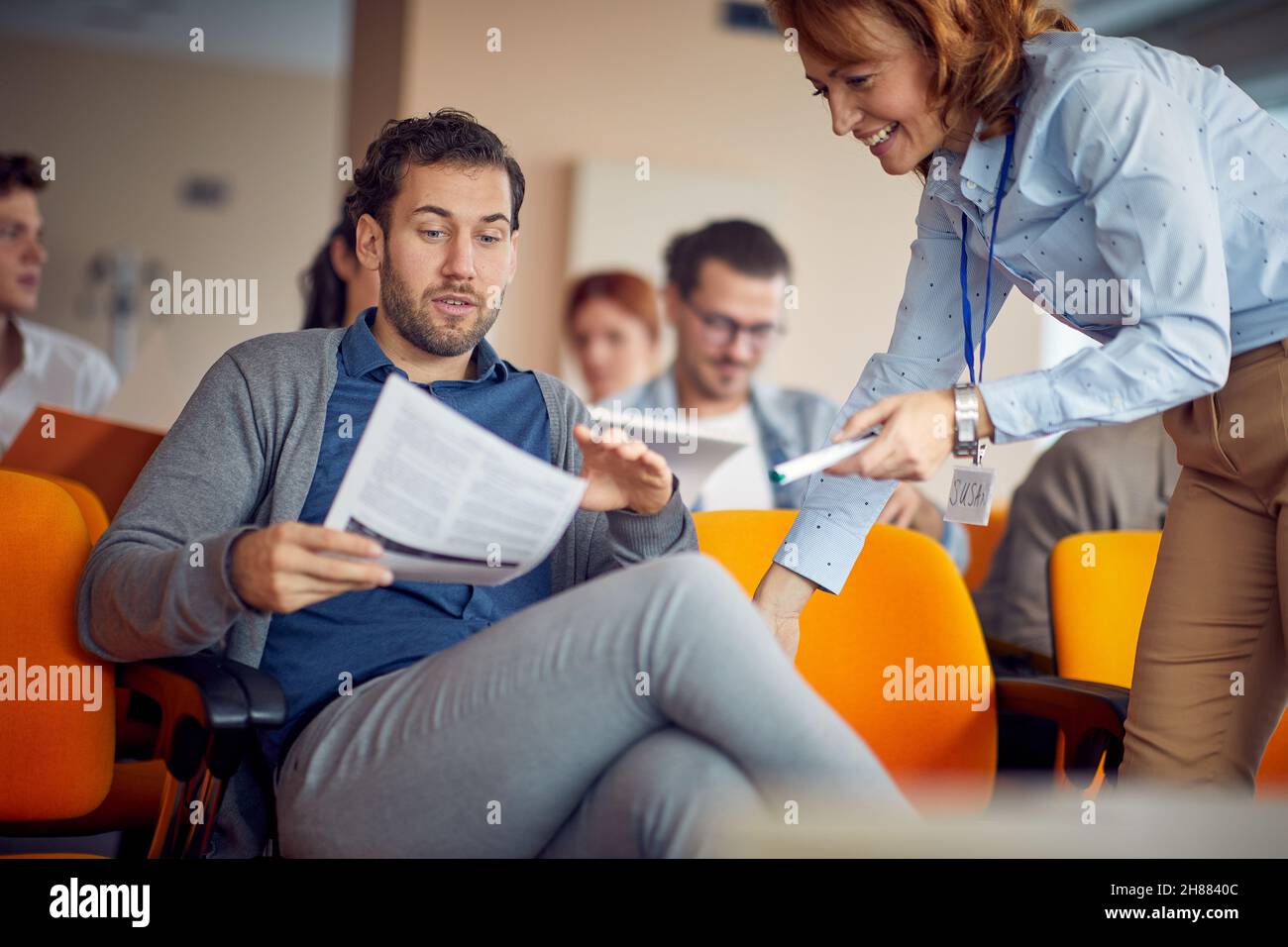 Ein junger männlicher Teilnehmer, der beim Business-Vortrag in entspannter Atmosphäre Hilfe vom Dozenten erbittet. Unternehmen, Leute, Meetings, Unternehmen Stockfoto