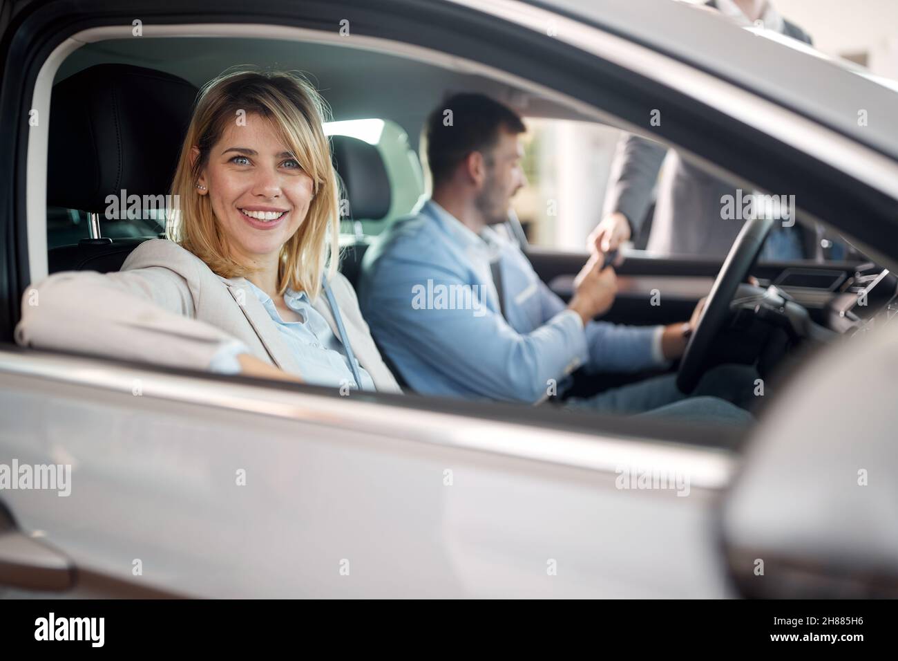 Glückliche Familie in einer aufgeregten Atmosphäre, die in dem neuen Auto sitzt, das sie in einem Autogeschäft gekauft haben. Auto, Geschäft, Kauf Stockfoto