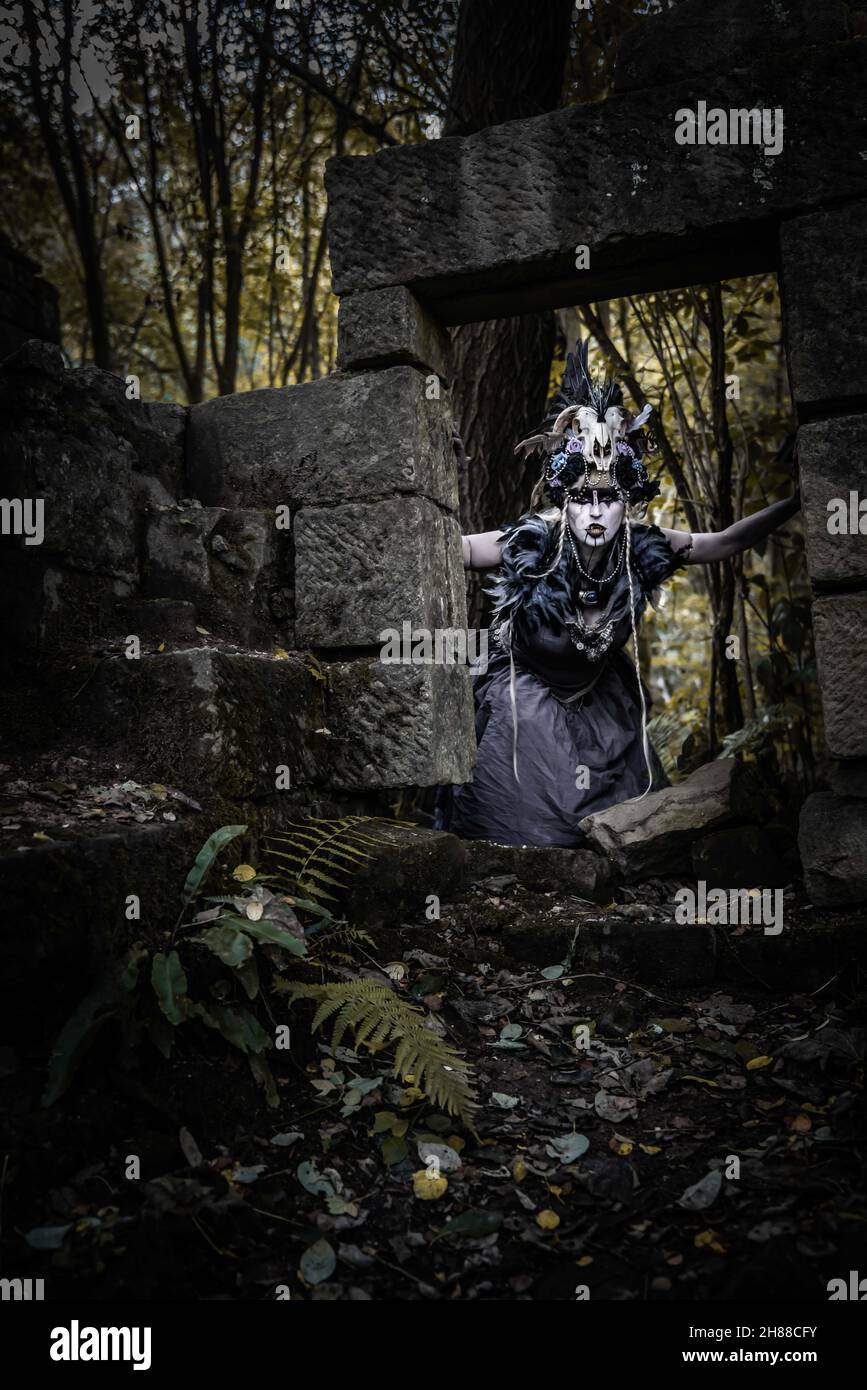 Die Vampirhexe auf dem Streifzug durch die Ruinen und Wälder. Ich trage ein zerrissenes Ballkleid und ein Schädelkopfkostüm Stockfoto