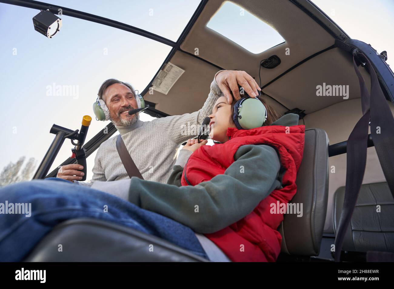 Aufmerksamer Pilot, der einem Kind mit einem Flugkopfhörer auf einem Hubschrauber hilft Stockfoto