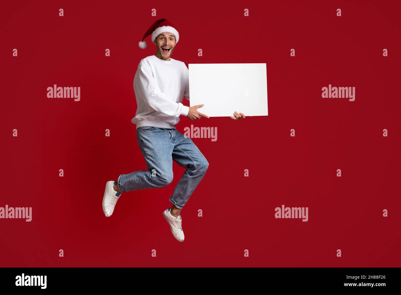 Sehen Sie Sich Das An. Überfröhter Mann Im Weihnachtsmütze, Der Mit Leerem Schild Springt Stockfoto