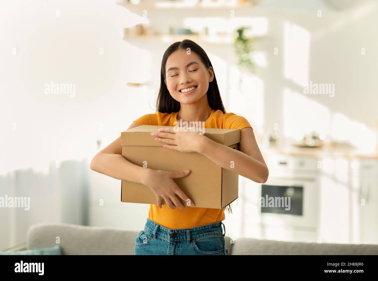 Überglücklich asiatische Dame umarmt Karton Paket, Erhalt lang erwartete Lieferung, immer online bestellen, zu Hause stehen Stockfoto