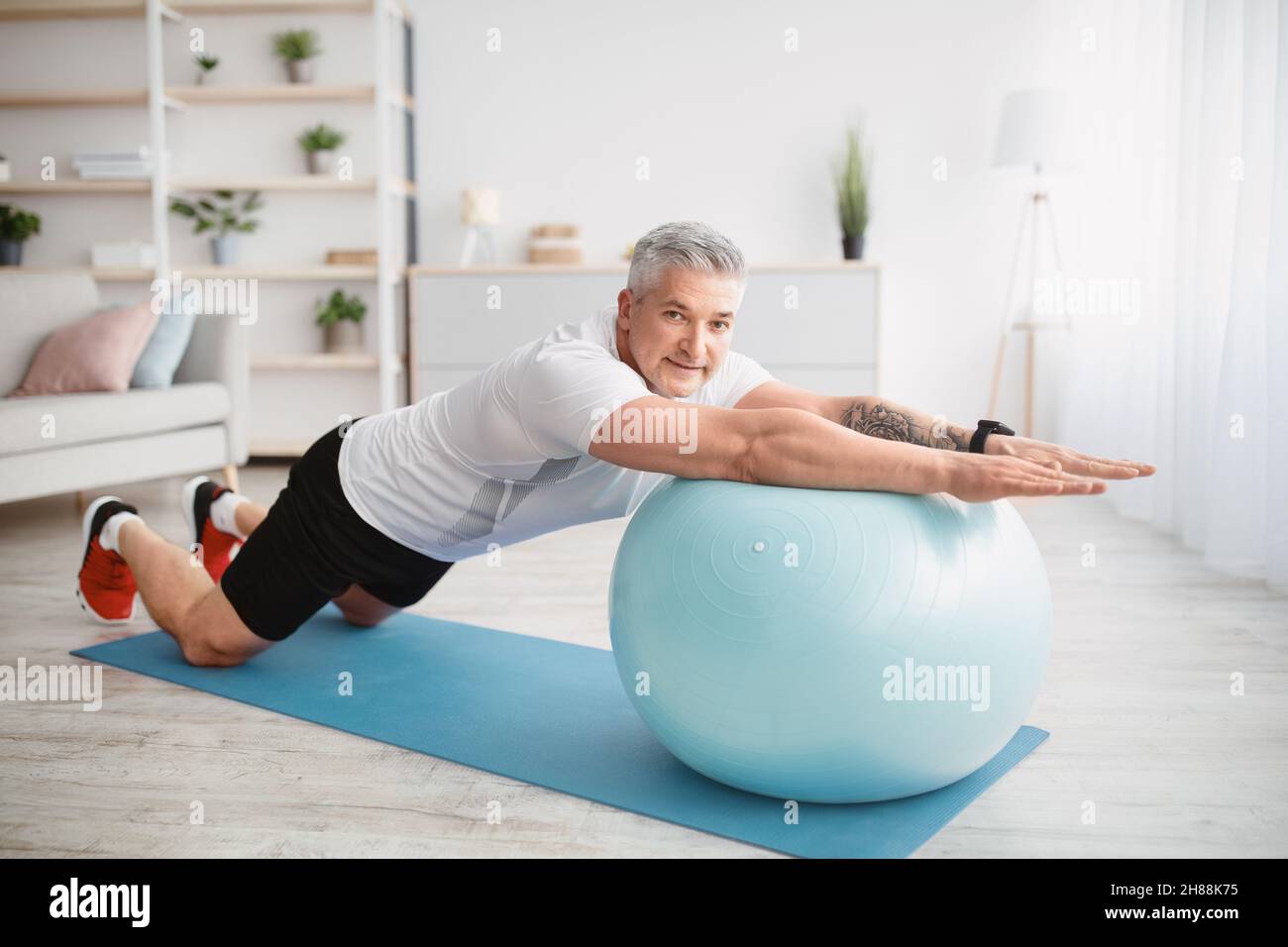 Home Workout-Konzept. Sportlicher älterer Mann, der mit einem Fitnessball trainiert und zu Hause die Kernmuskeln trainiert Stockfoto