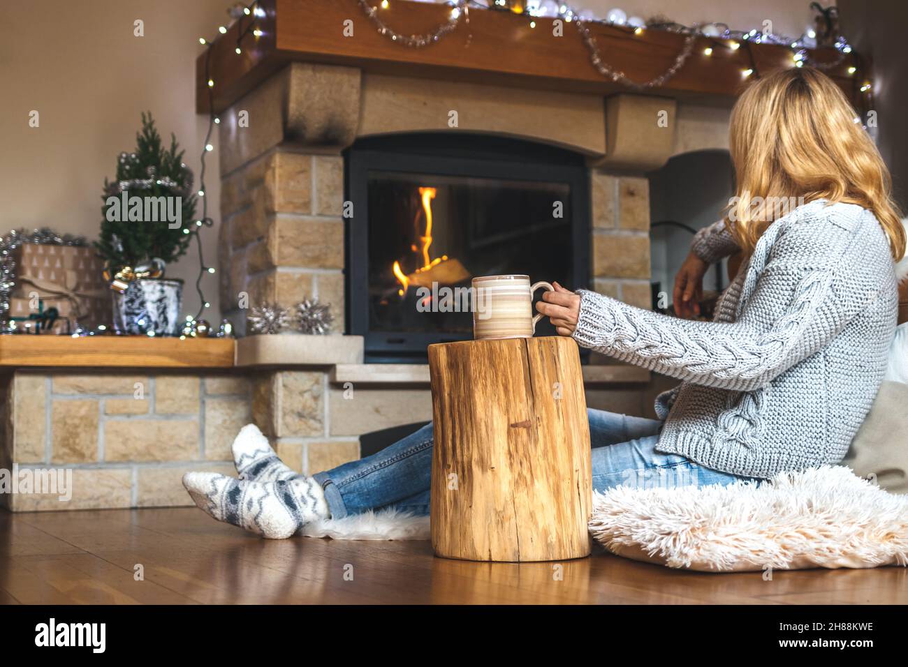 Entspannung während des weihnachtsaufkommens. Frau trinkt Kaffee vor dem  Kamin im skandinavischen Zuhause. Baumstumpf als Beistelltisch aus Holz  Stockfotografie - Alamy