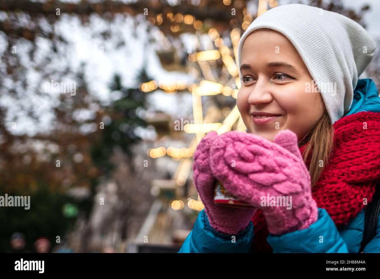 Junge Frau trinkt Glühwein auf dem weihnachtsmarkt am Rathausplatz, Wien, Österreich. Fröhlicher Tourist, der während der weihnachtsferien Urlaub genießt Stockfoto