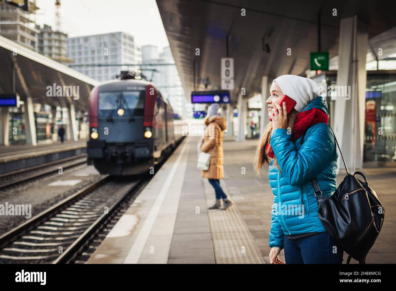 Fahrgäste am Bahnhof Rairoad und ankommendem Zug. Frau, die vor der Reise ein Smartphone benutzt. Öffentliche Verkehrsmittel in der Stadt Stockfoto