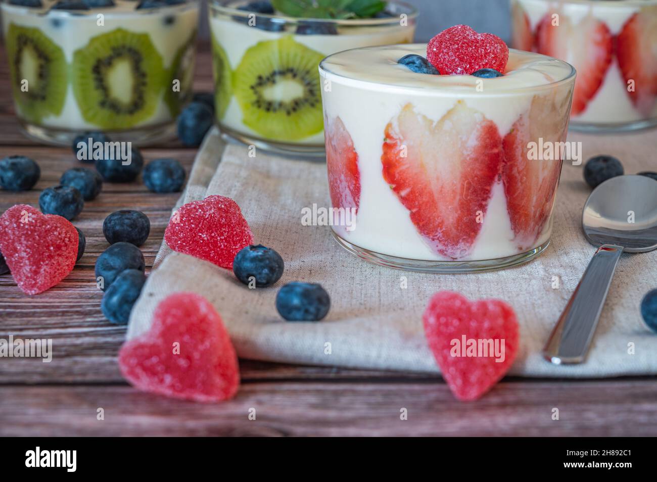 Hausgemachtes gesundes Frühstück in einem Glas mit frischen Früchten: Kiwi, Erdbeere und Joghurt auf Holzgrund. Geringe Schärfentiefe mit selektivem FOC Stockfoto
