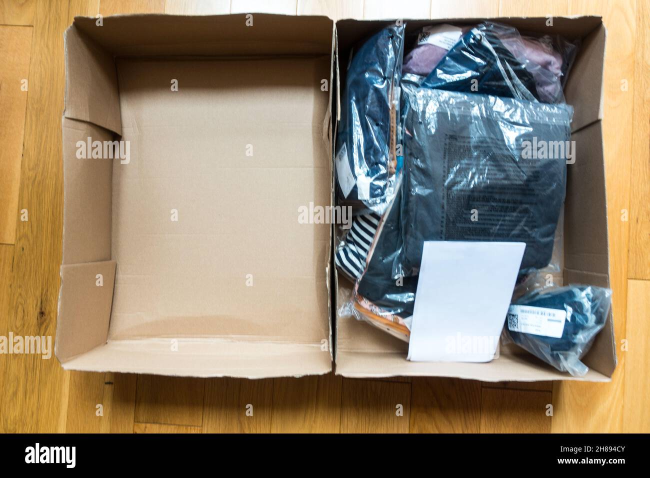 Das Modelabel H&M versendet Pakete in einer Pappschachtel mit individueller Kleidung, die in Kunststoff verpackt ist Stockfoto