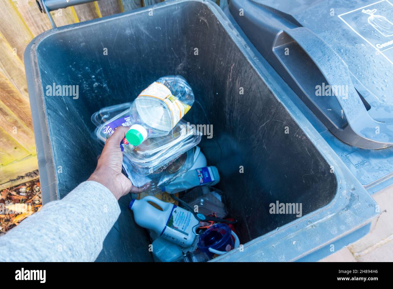 Erwachsene männliche Hand Fallenlassen von Plastikgegenständen in einen großen grauen Abfallbehälter zum Recycling Stockfoto