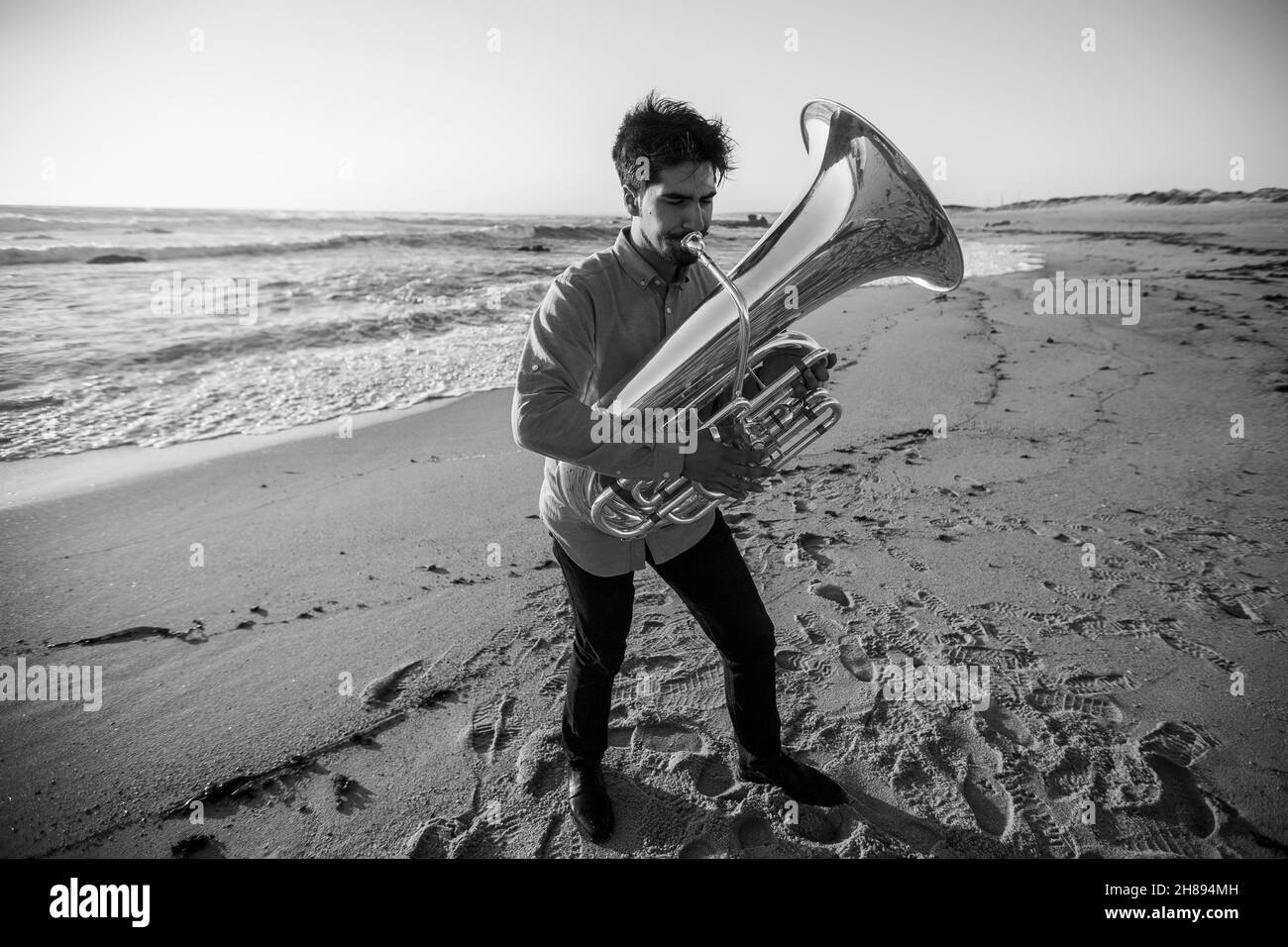 Mann Musiker spielt die Tuba in der Nähe des Ozeans. Schwarzweiß-Foto. Stockfoto
