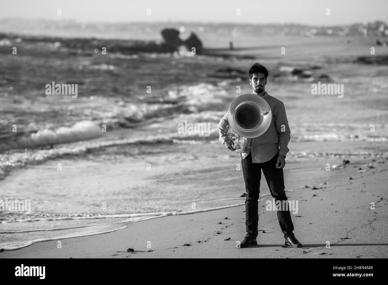 Musiker, der mit einer Tuba in der Nähe des Ozeans steht. Schwarzweiß-Foto. Stockfoto