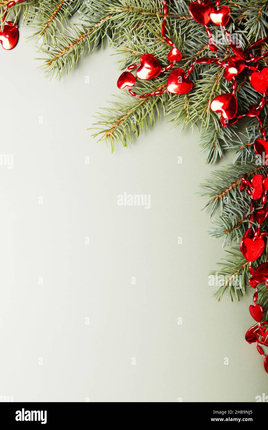 Weihnachtskonzept, grüne Kiefernzweige mit kleinen roten Herzen Dekor auf hellgrünem Hintergrund. Leerer Raum für Text. Stockfoto