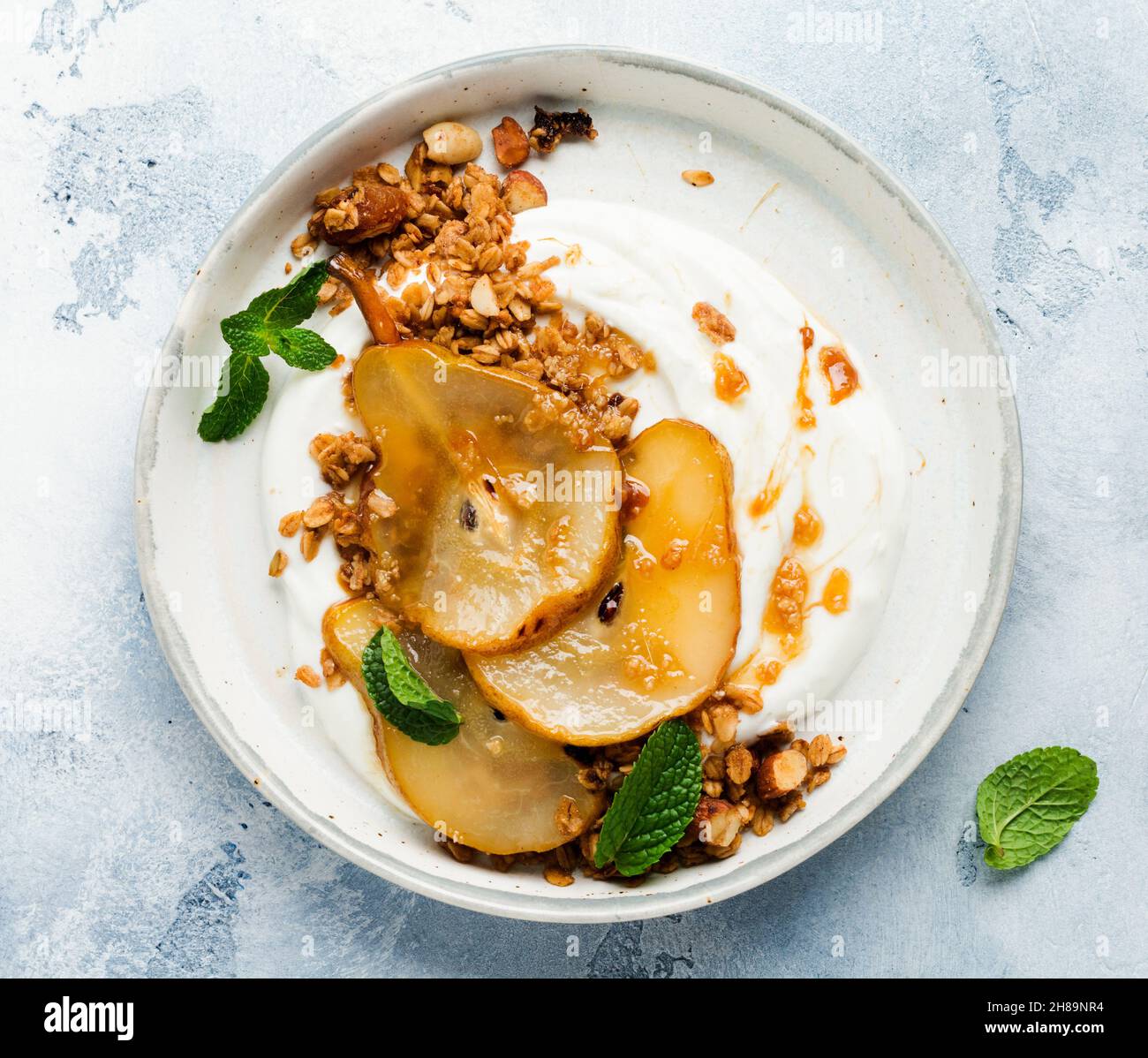 Griechischer Joghurt mit karamellisierter Birne, Müsli, Nüssen und geschmolzenem Zucker für ein gesundes Frühstück auf einer grauen Keramikplatte. Rustikaler Stil. Draufsicht. Stockfoto