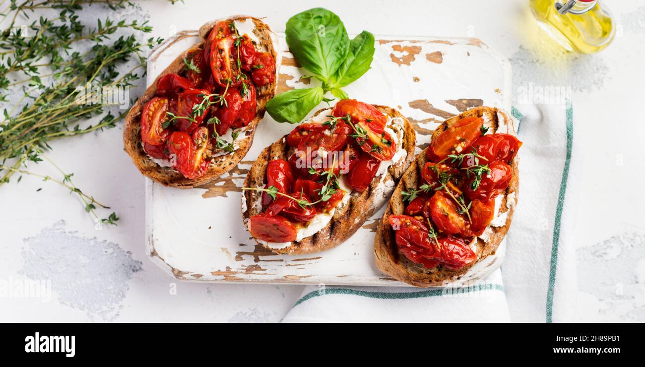 Sandwiches mit gebackenen Kirschtomaten und Quark, Thymian, Knoblauch und Kräutern auf einem alten, leichten Vintage-Hintergrund. Draufsicht. Stockfoto