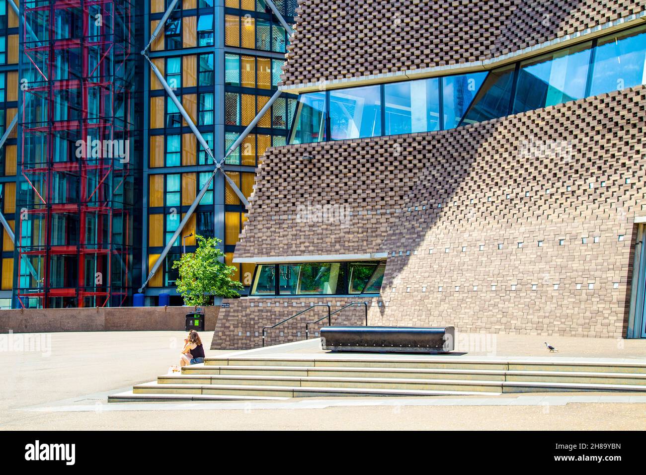 Frau, die vor dem Tate Modern Blavatnik Building, Bankside, London, Großbritannien, sitzt Stockfoto