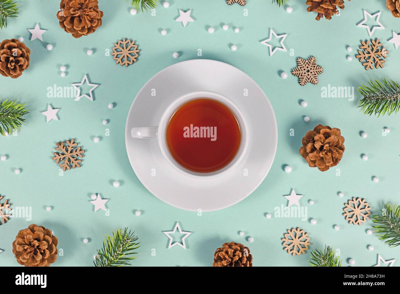 Tasse mit rotem Tee, umgeben von saisonaler Winterdekoration auf mintgrünem Hintergrund Stockfoto