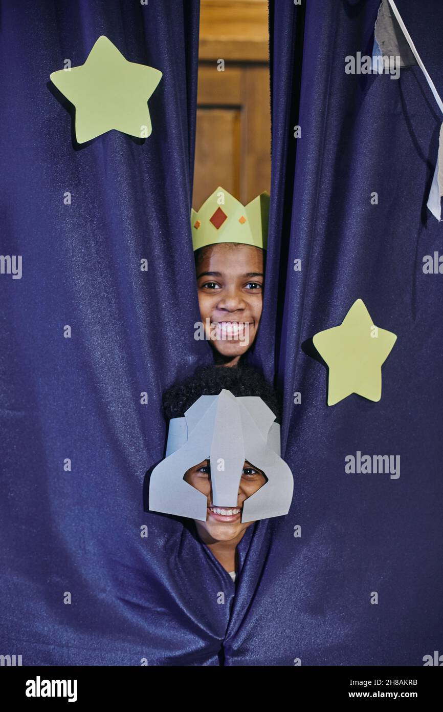 Nette glückliche Junge und Mädchen in Bühnenkostümen von Ritter und Prinzessin aus blauen Vorhängen mit Sternen verziert gucken Stockfoto