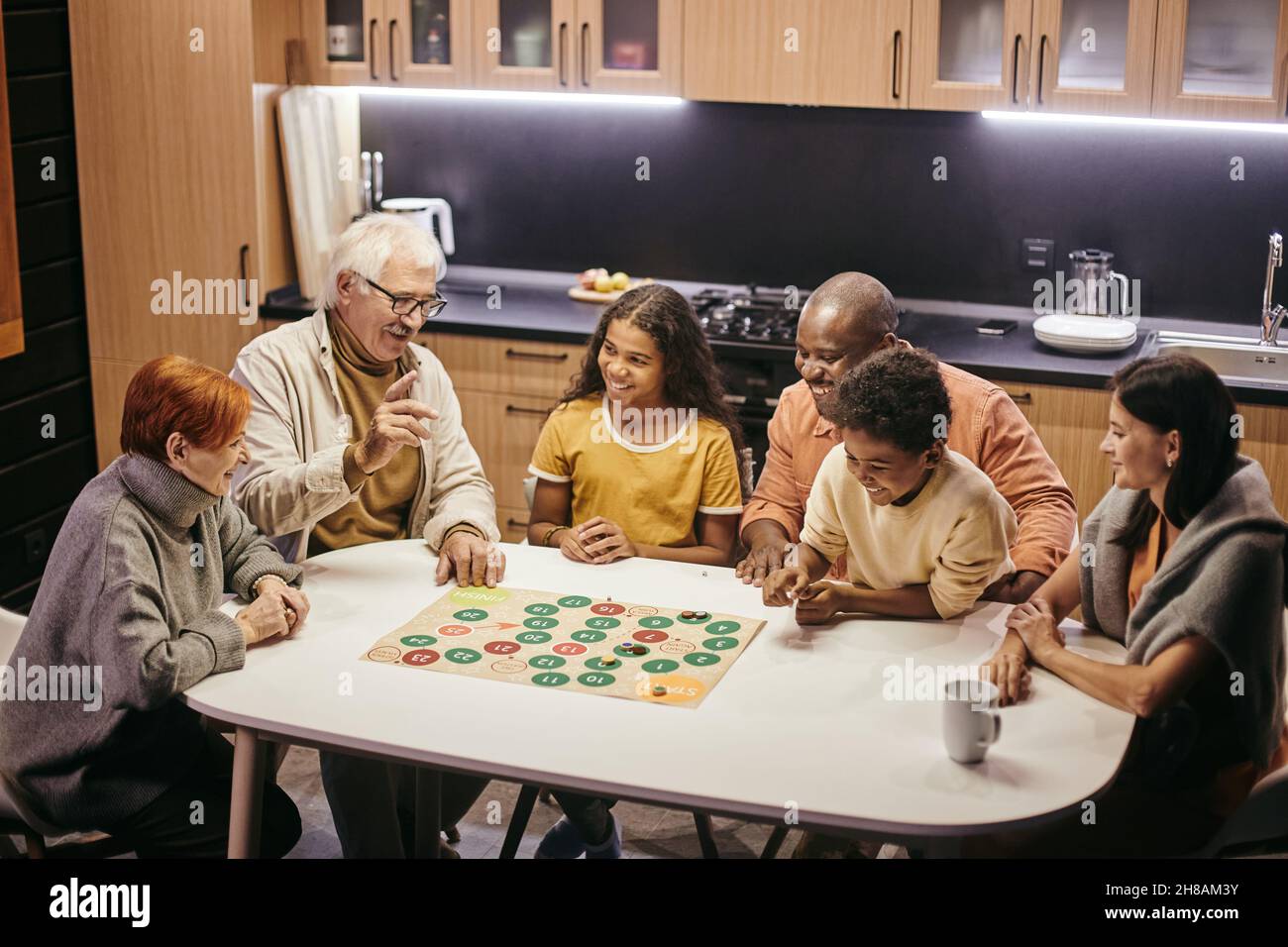 Große glückliche multirassische Familie aus drei Generationen, die Brettspiel spielt, während sie am Tisch in der Küche sitzt Stockfoto