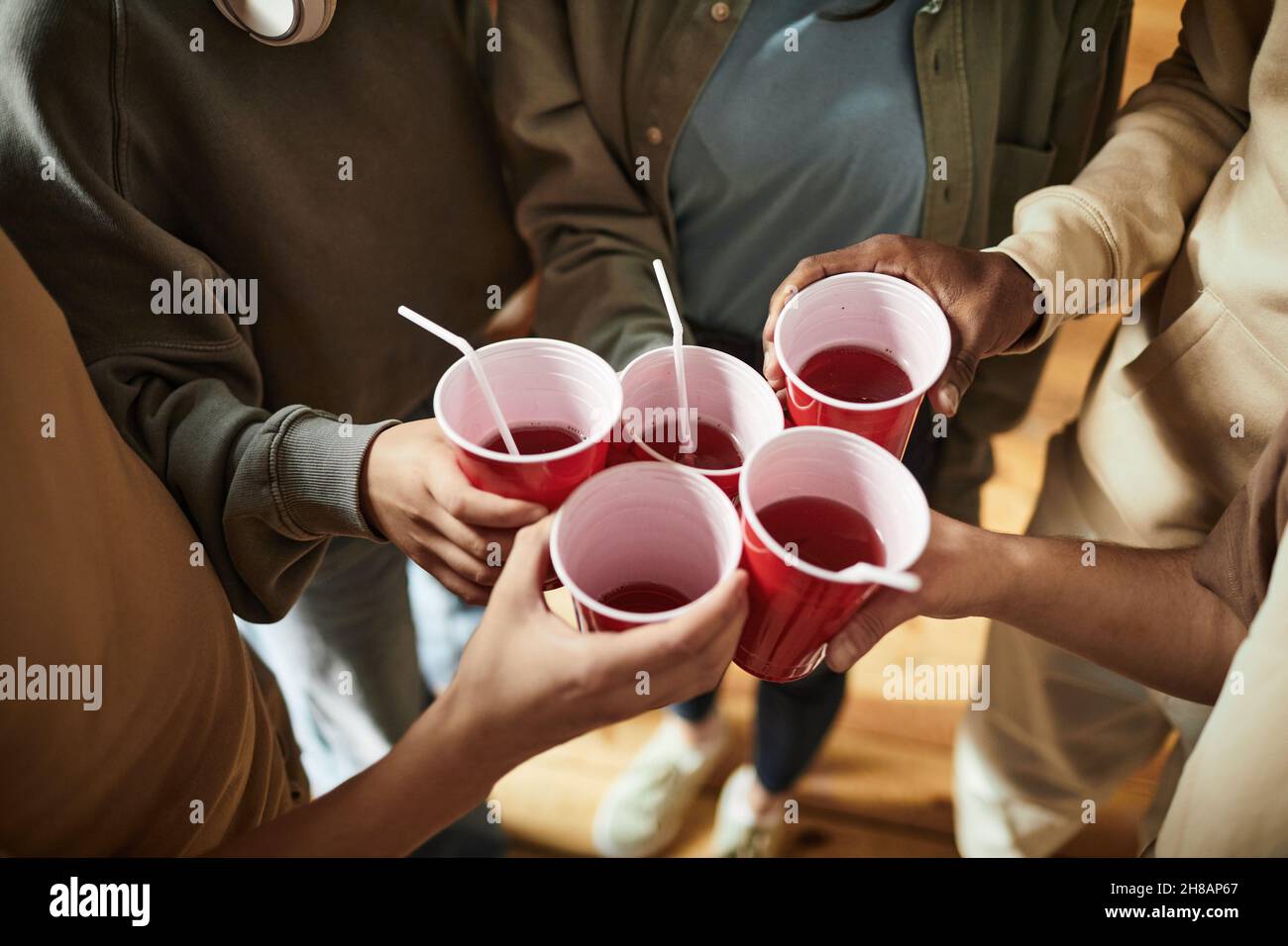 Nahaufnahme von jungen Leuten, die auf einer Party mit Plastikbechern und alkoholischen Getränken toasten Stockfoto