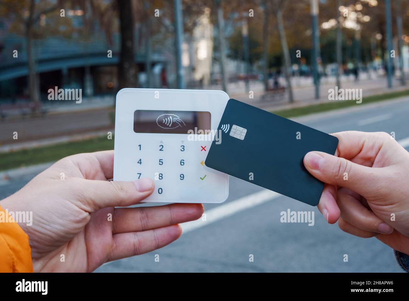 Weibliche Kundin ohne Gesicht, die NFC-Kauf mit Plastikkarte auf dem Terminal in der Stadtstraße macht Stockfoto