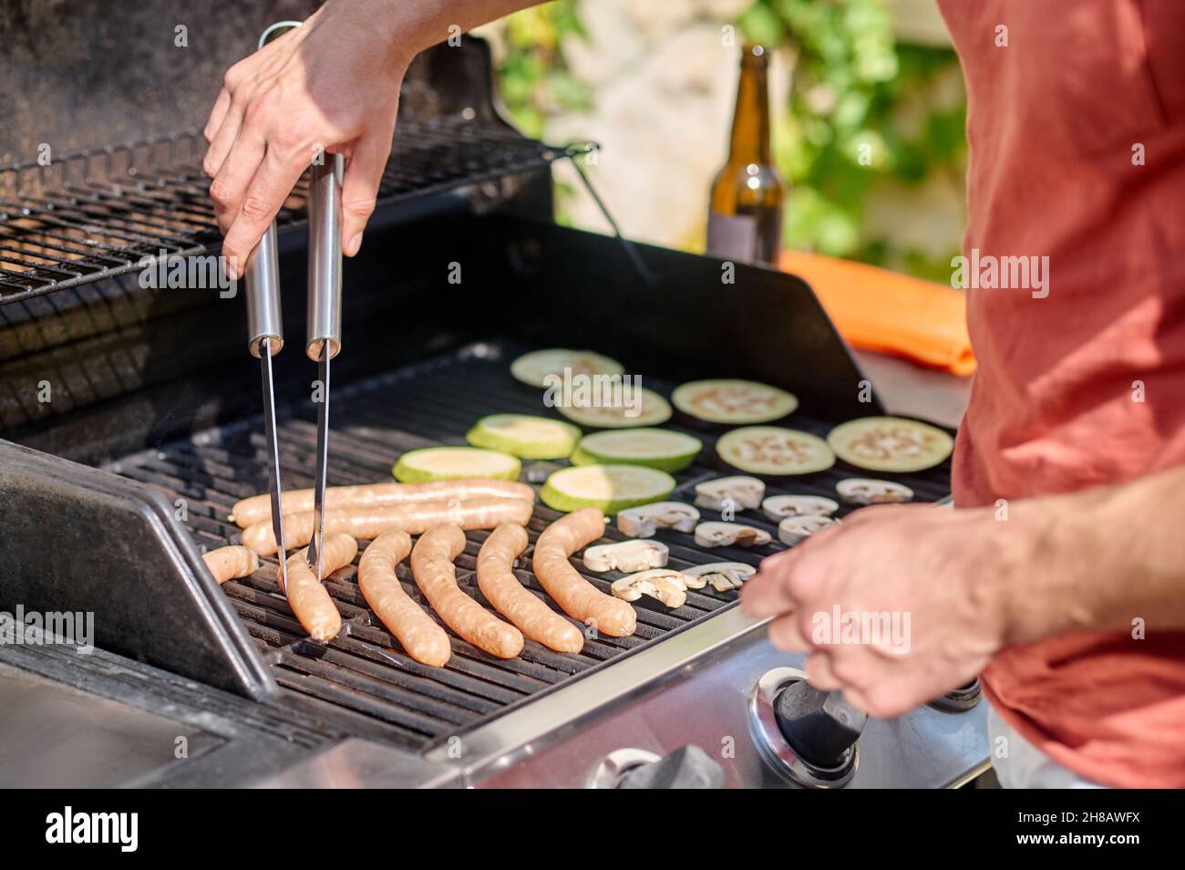 Ein Mann, der gegrillte Würstchen und Gemüse kocht Stockfoto