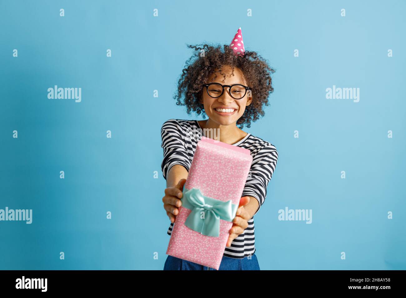 Fröhliche Frau im Geburtstag Kegelhut hält Geschenk Stockfoto