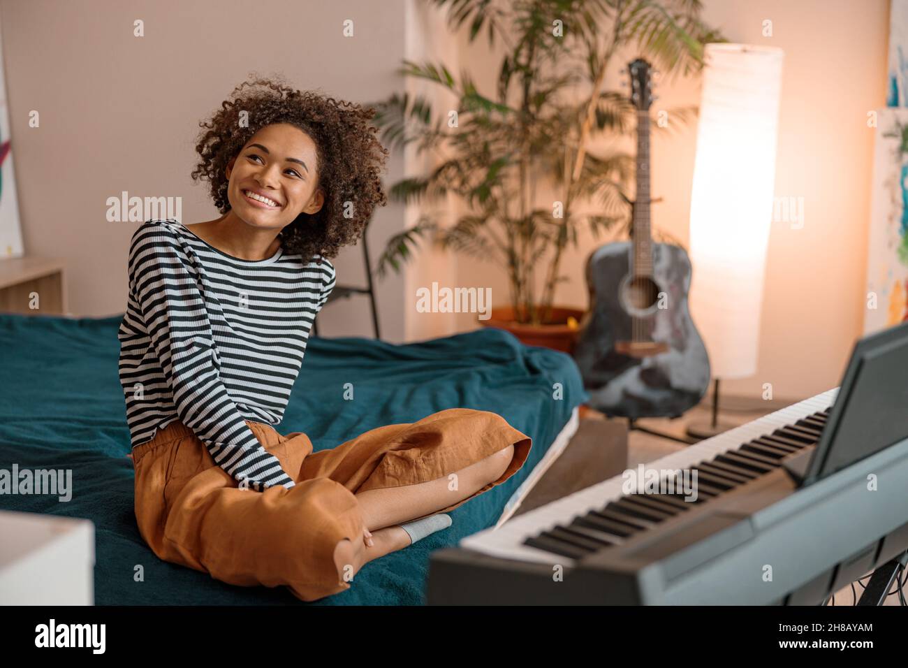 Fröhliche afrikanische Frau, die zu Hause in der Nähe des Synthesizers sitzt Stockfoto