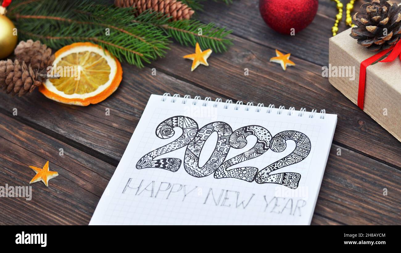 Frohes neues Jahr. Das Jahr 2022, geschrieben in einem Notizbuch, das auf einem festlich geschmückten Holzhintergrund liegt, selektiver Fokus. Neujahrsfeiertagskonzept. Stockfoto