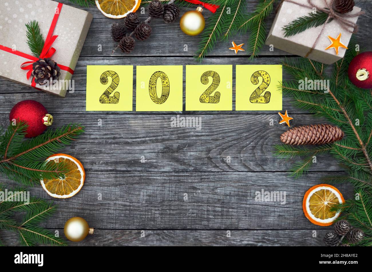 Gelbe Haftnotizen mit Zahlen 2022 auf festlichem Holzhintergrund mit Kopierfläche. Neujahrskomposition mit Geschenkkartons, Tannenzweigen, Zapfen und de Stockfoto