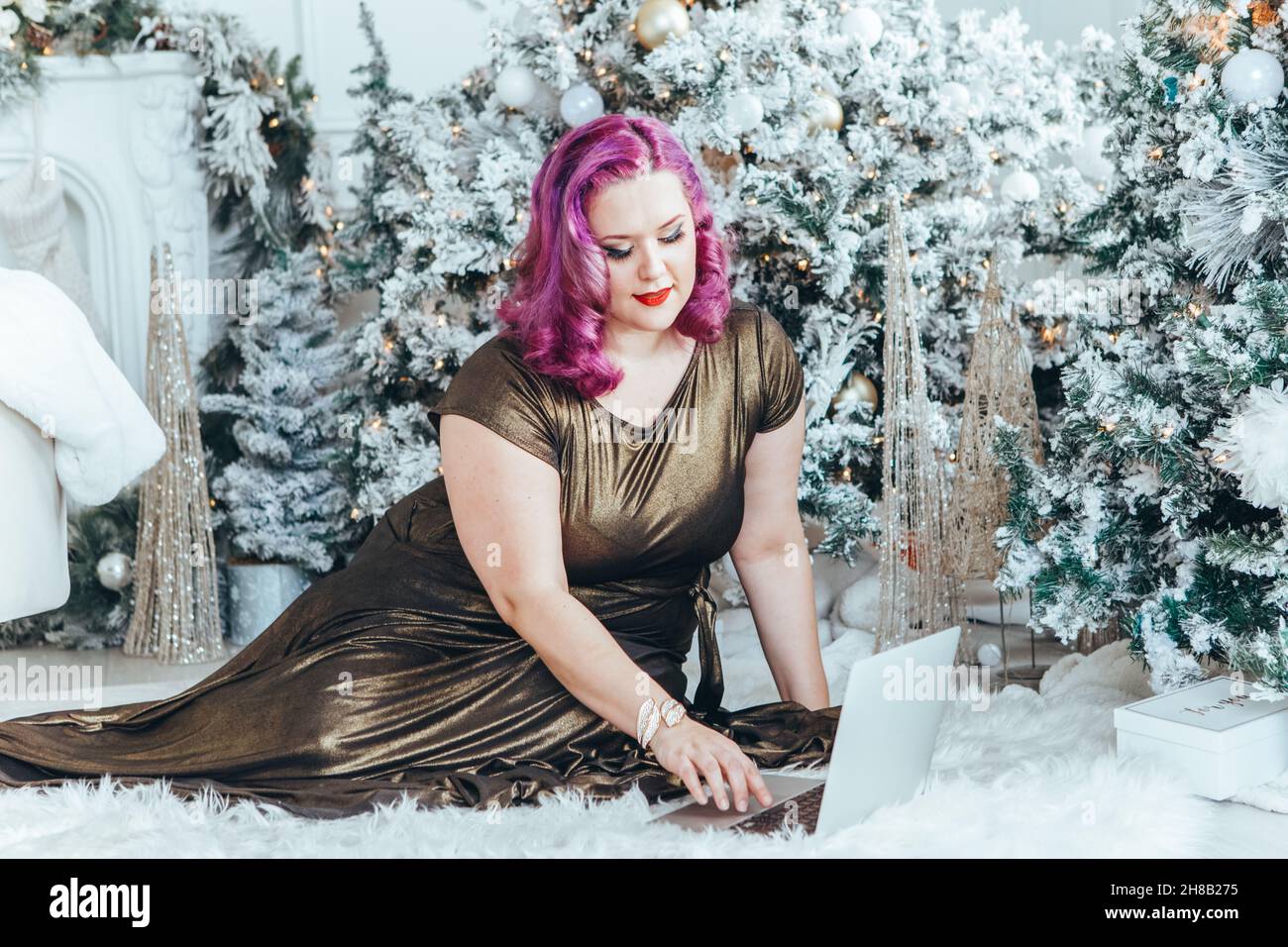 Schöne junge kaukasische Plus Größe Modell Frau in langen goldenen Kleid Aufruf auf Laptop online und chatten mit Familienfreunden zu Weihnachten oder New Yea Stockfoto