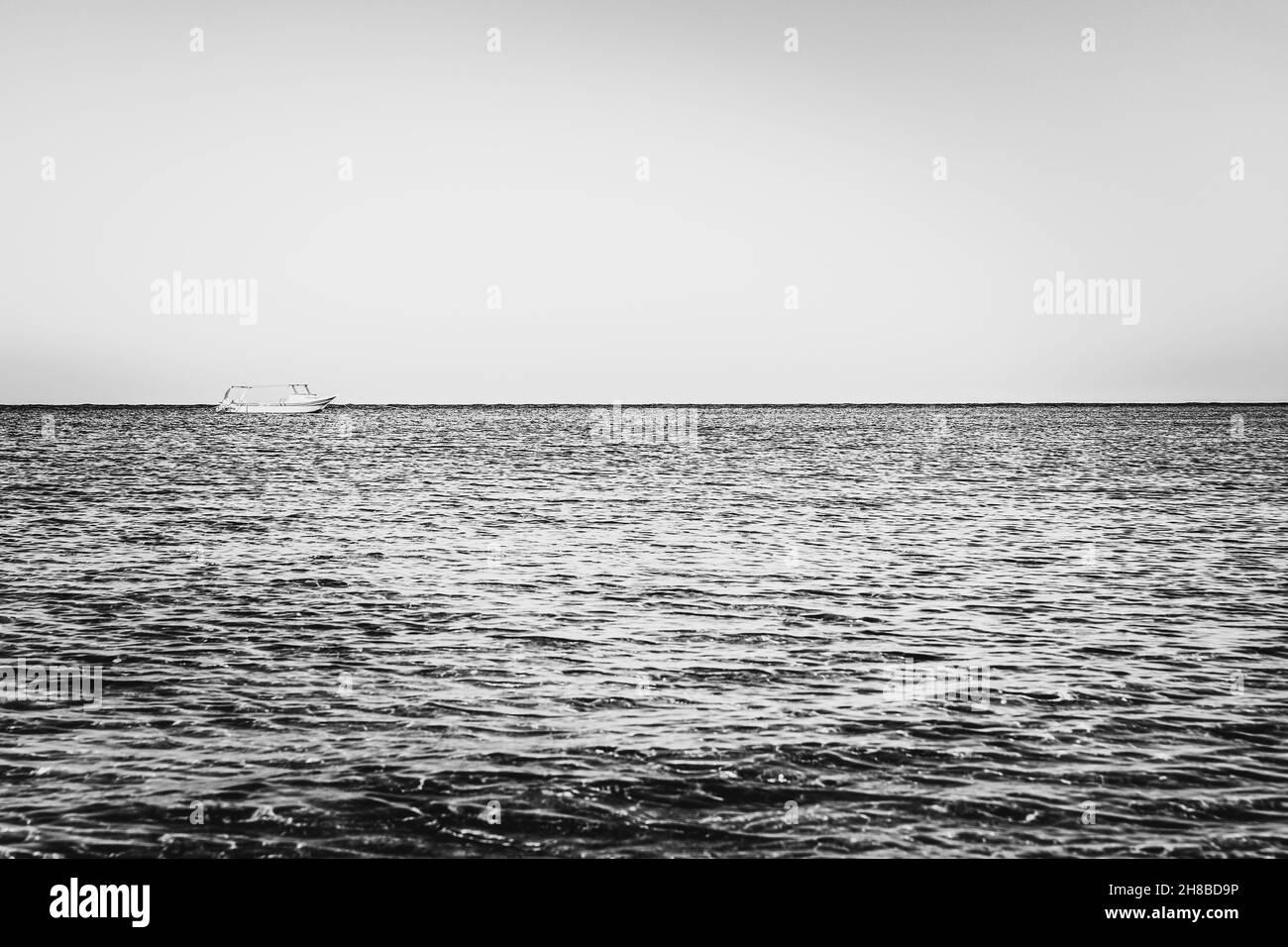Schwarzweiß-Fotografie. Allein verschwommenes Boot oder Schiff in stillem Meer oder Meerwasser Stockfoto