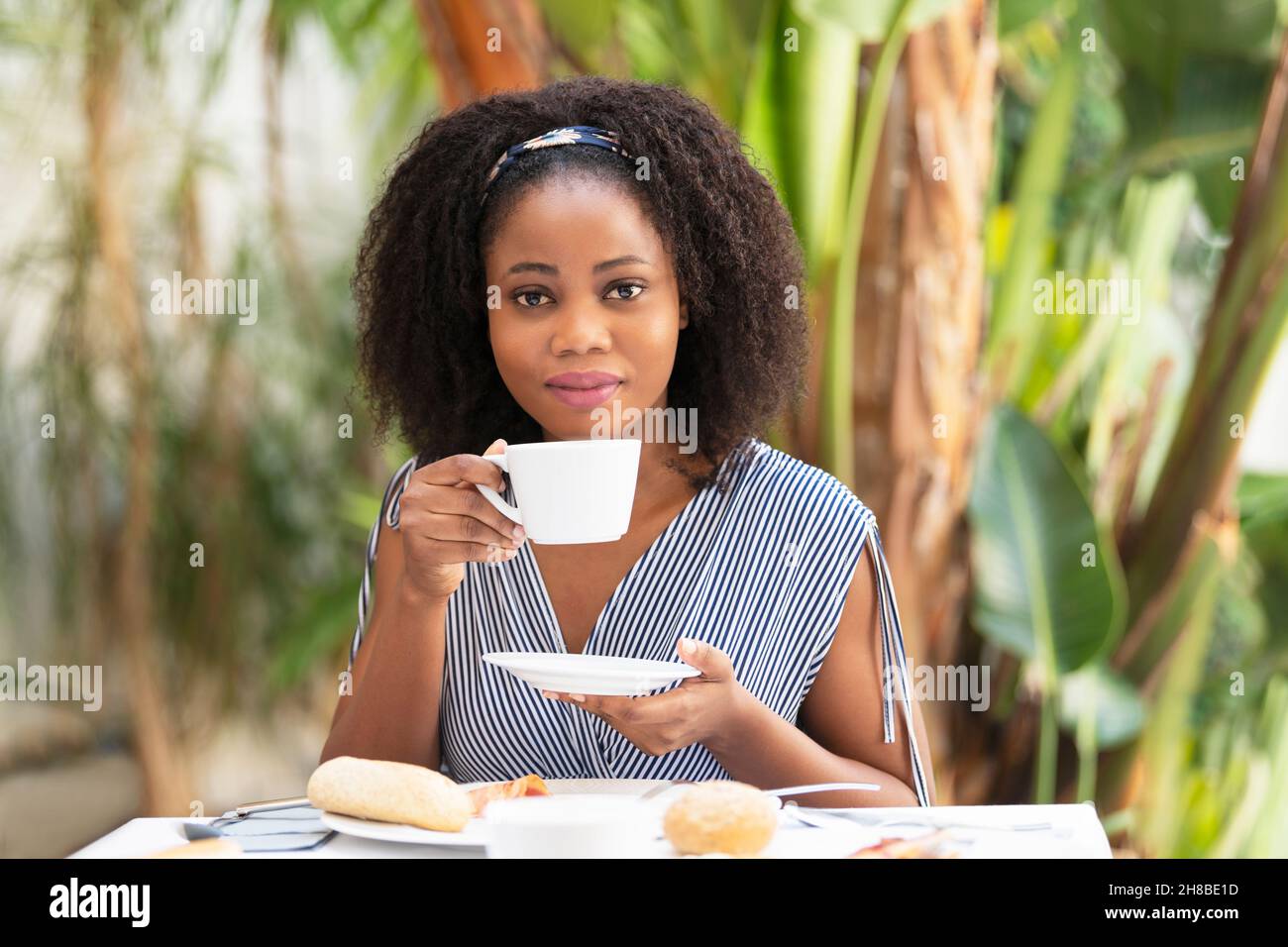 Eine afroamerikanische junge Frau, die eine Tasse Kaffee in einem Café vor der Tür hält Stockfoto