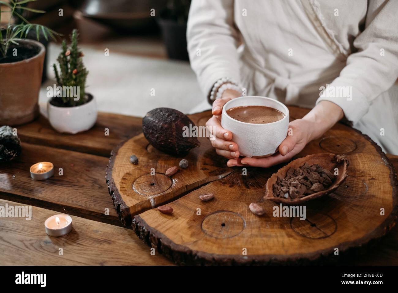 Heißer handgemachter zeremonieller Kakao in weißer Tasse. Frau Hände halten Handwerk Kakao, Draufsicht auf Holztisch. Bio gesundes Schokoladengetränk aus zubereitet Stockfoto