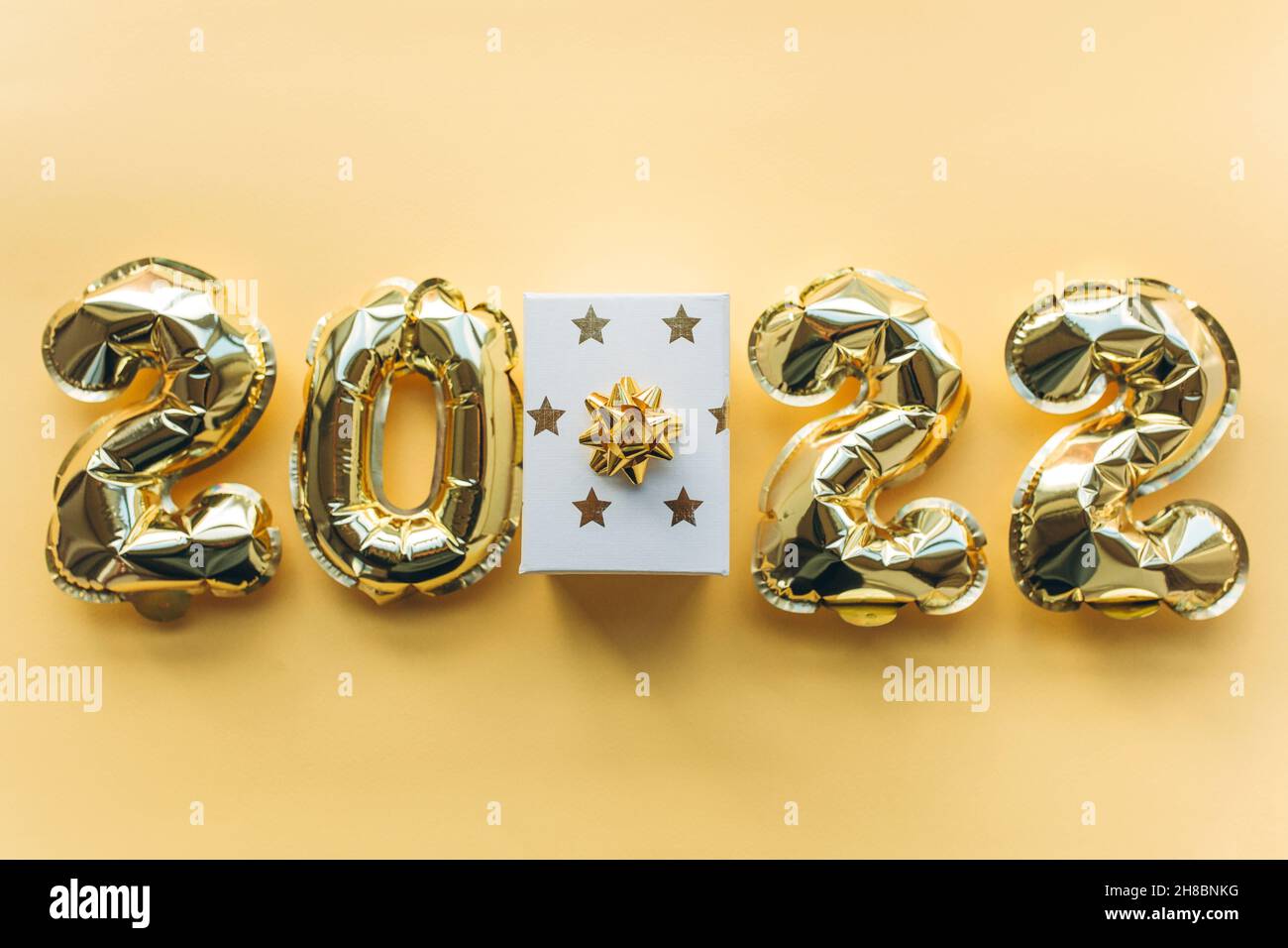 Luftballons aus Goldfolie in Form von Zahlen 2022 und Geschenkbox auf einem goldenen Hintergrund. Stockfoto