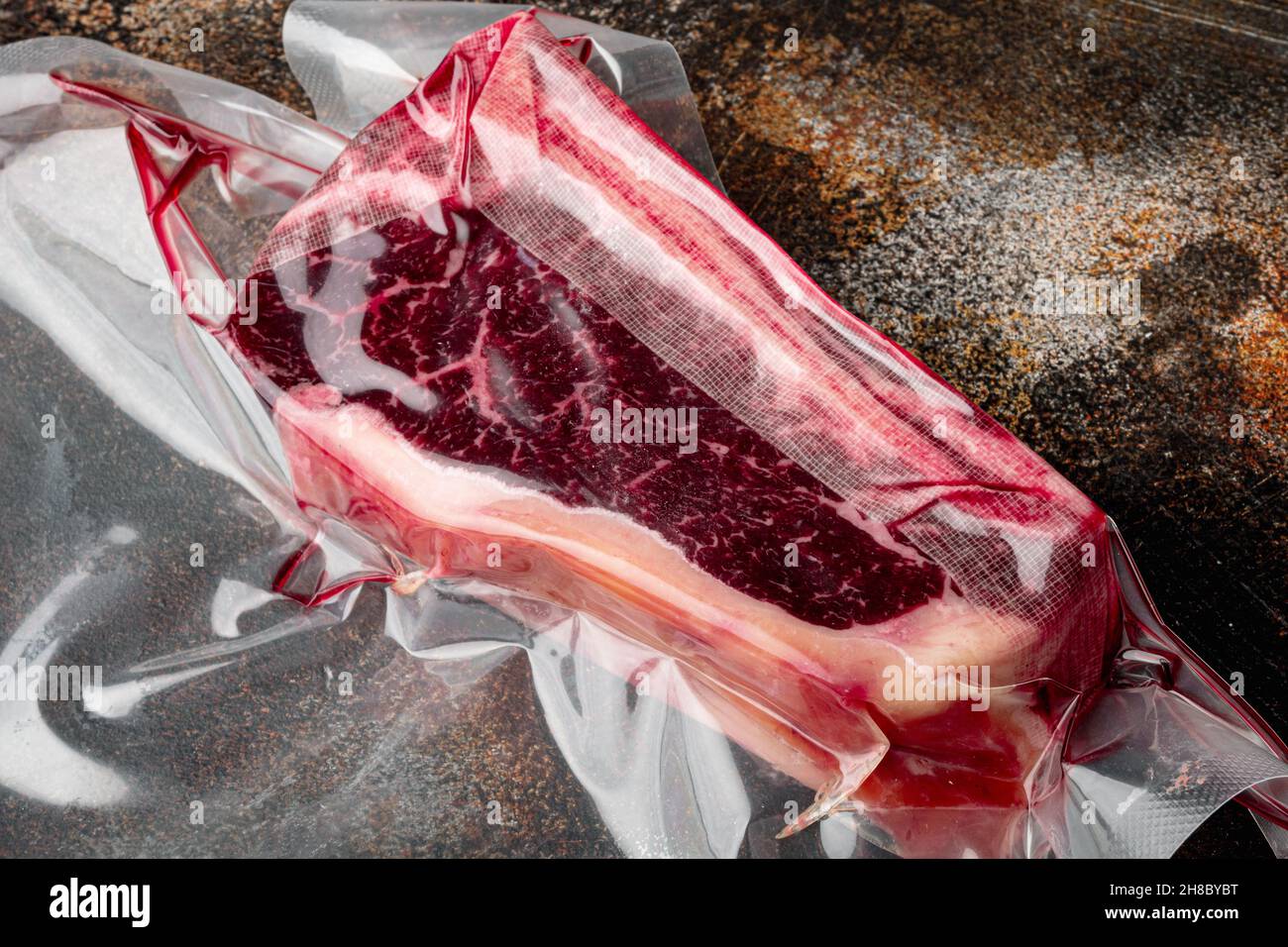 Frisches, riesiges und appetitliches Clubsteak im Vakuumverpackungsset, auf altem dunklen rustikalen Hintergrund Stockfoto