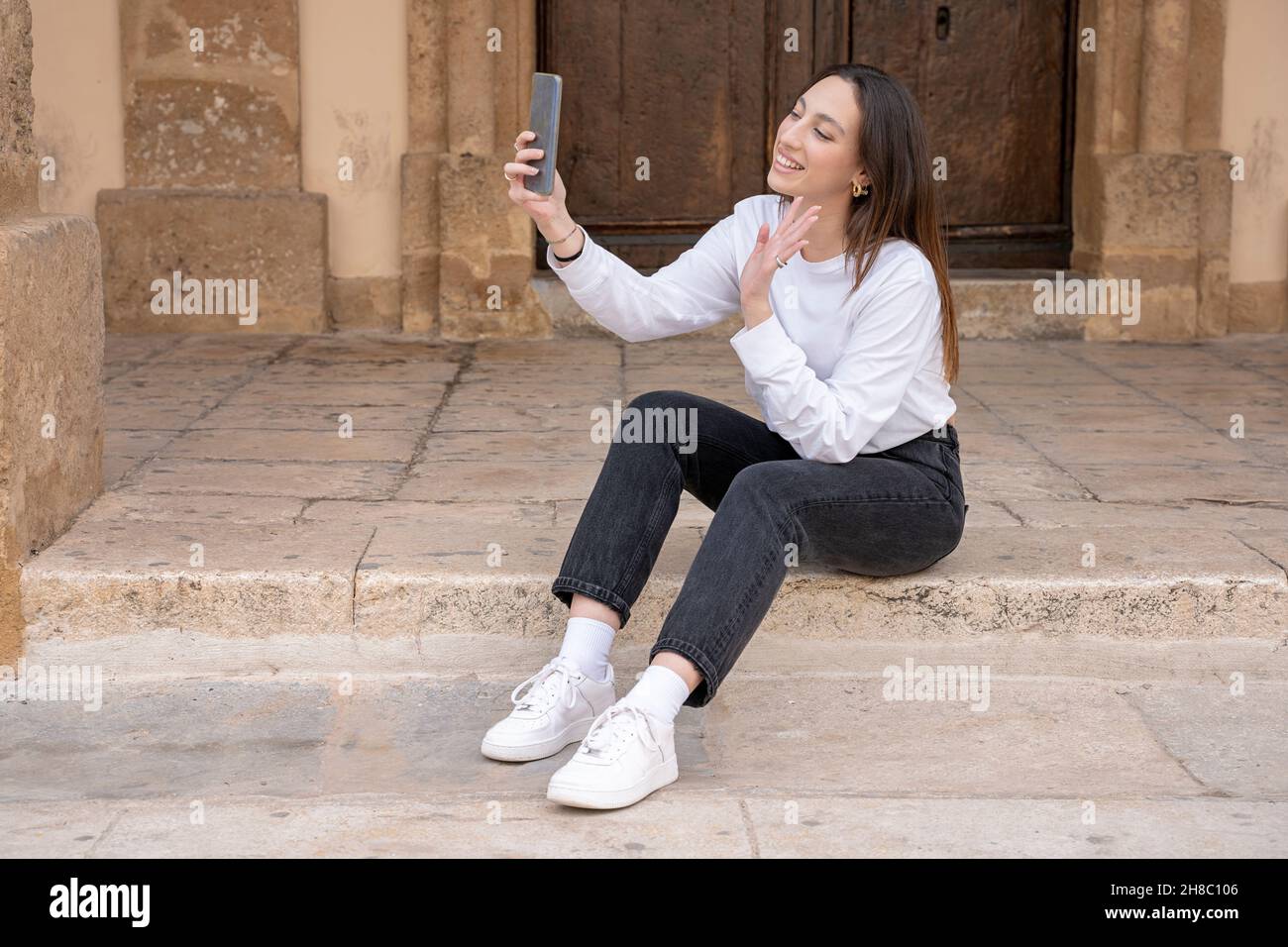 Junge lächelnde Frau sitzt Datum Videoanruf mit Handy im Freien Stockfoto