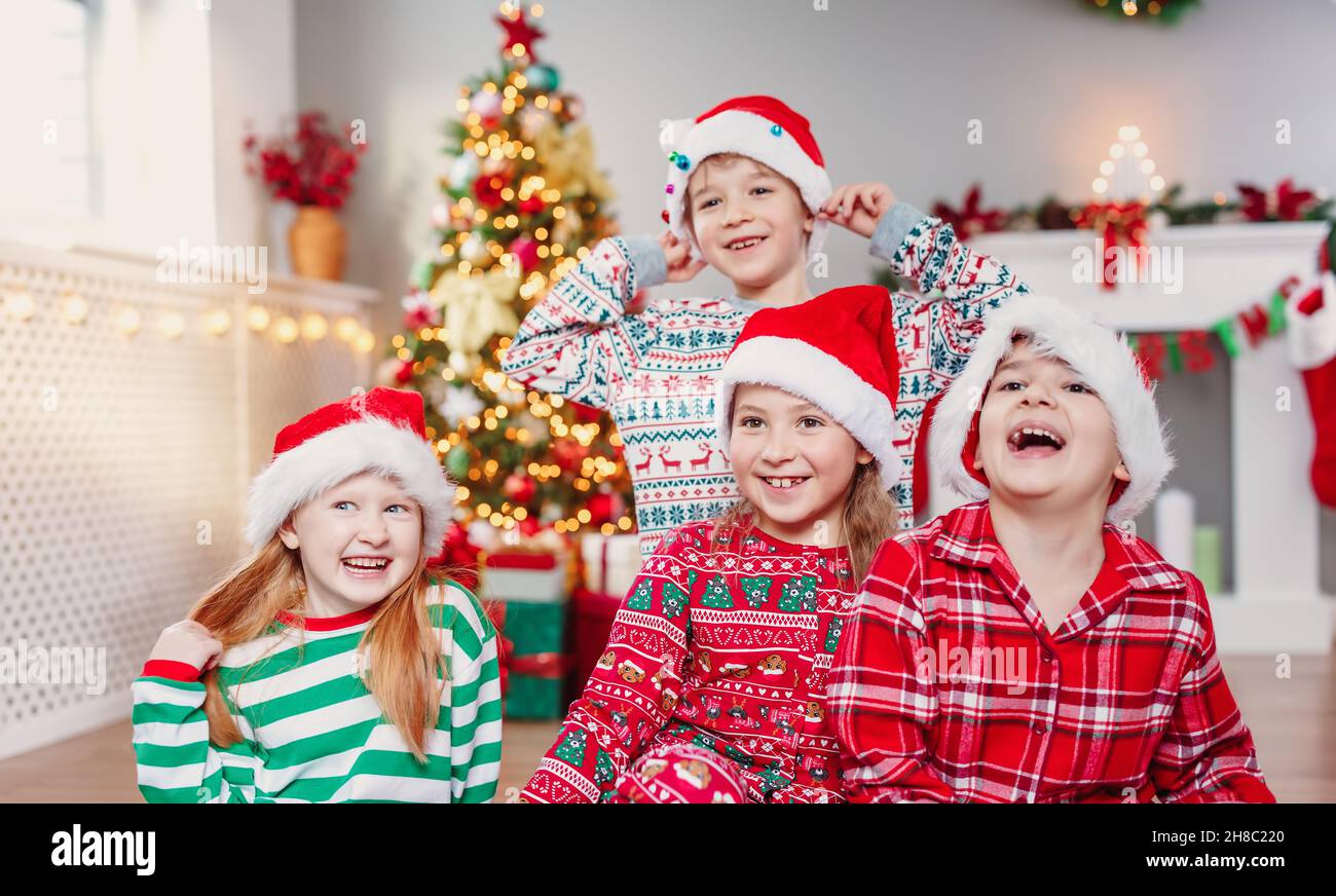 Fröhliche Kinder sitzen im Wohnzimmer zu Hause in weihnachten Pyjamas Stockfoto