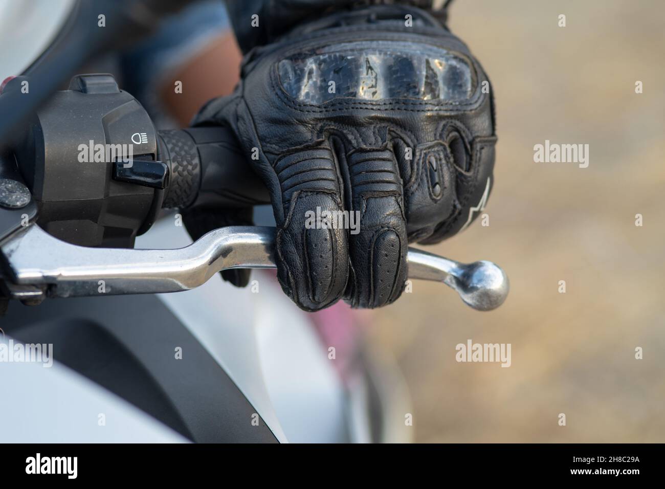 Detail der linken Hand eines Bikers mit einem schwarzen Lederhandschuh am Kupplungshebel seines Motorrads Stockfoto