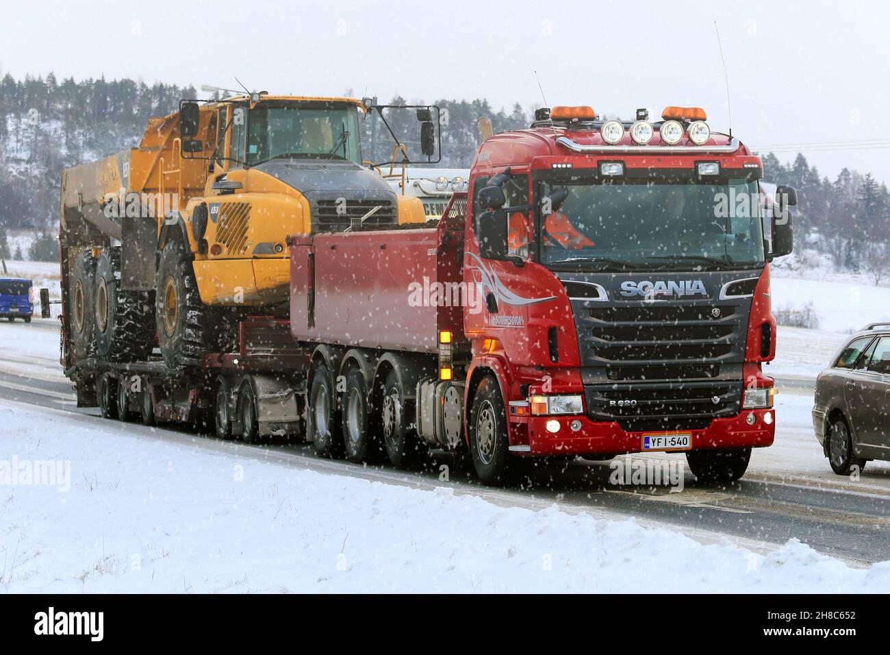 Red Scania R620 Schottertruck schleppt im Winter bei Schneefall den Sattelkipper Volvo A35D auf dem Anhänger entlang der Straße. Salo, Finnland. 15. Januar 2016. Stockfoto