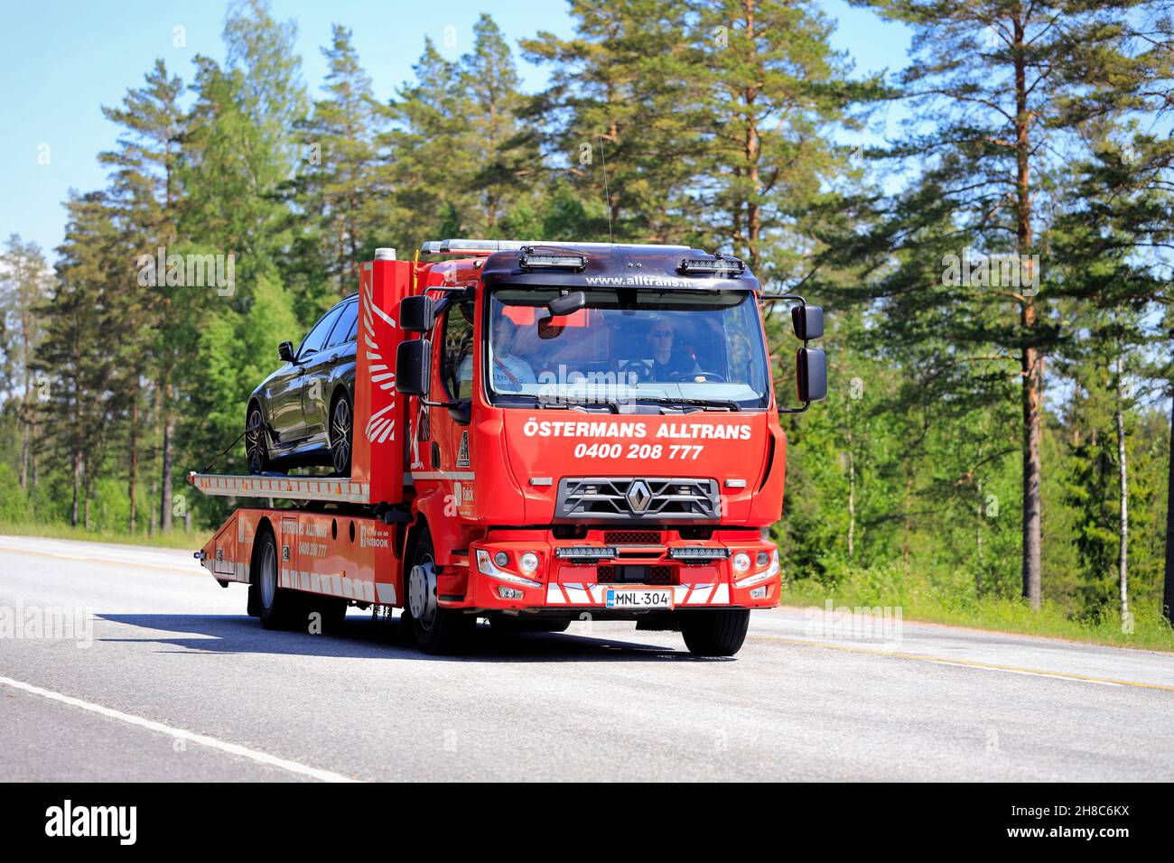 Renault-Flachbett-Rückgewinnungsfahrzeug von Ostermans ALLTRANS ab Oy, das an einem sonnigen Tag ein beschädigtes Auto entlang der Autobahn trägt. Raasepori, Finnland. 10. Juni 2021. Stockfoto