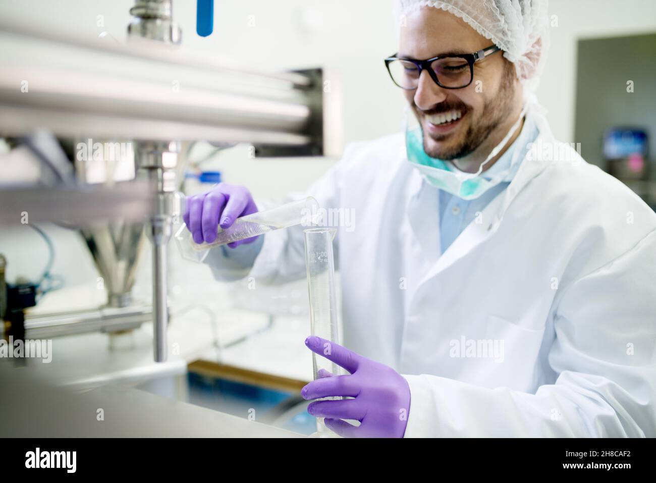 Lächelnder Labortechniker, der Wasseranalysen in steriler Schutzausrüstung macht. Stockfoto