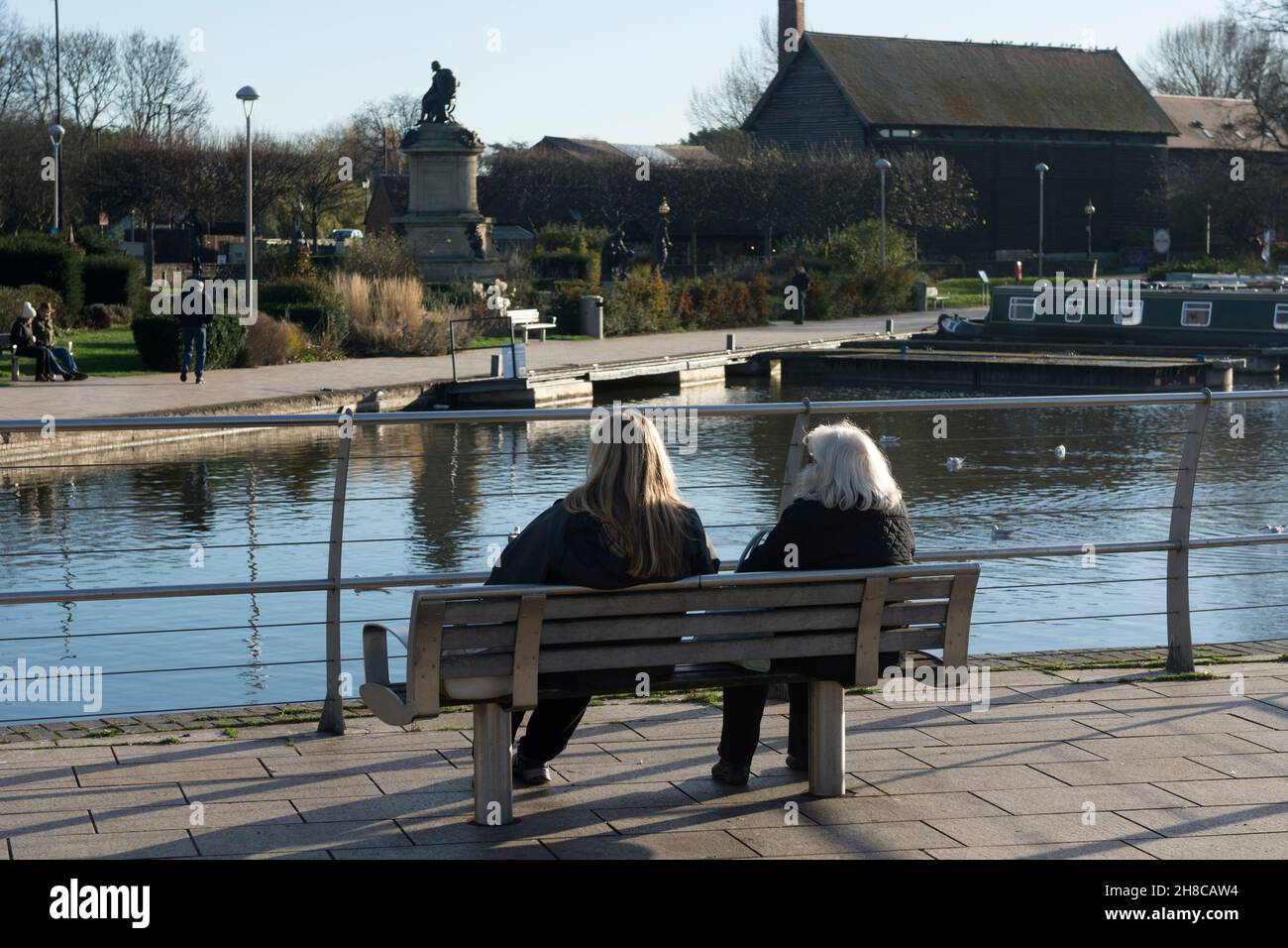 Zwei Frauen saßen auf einer Bank mit Blick auf das Kanalbecken von Bancroft Gardens, Stratford-upon-Avon, Warwickshire, England, Großbritannien. November 2021. Stockfoto