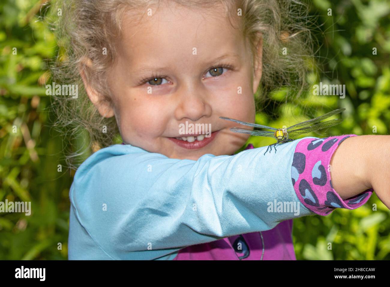 Blaugrüner Darner, südliche aeshna, südlicher Falkner (Aeshna cyanea), kleines lächelndes Mädchen mit einer Falkerin Libelle auf ihrem Arm, Deutschland Stockfoto