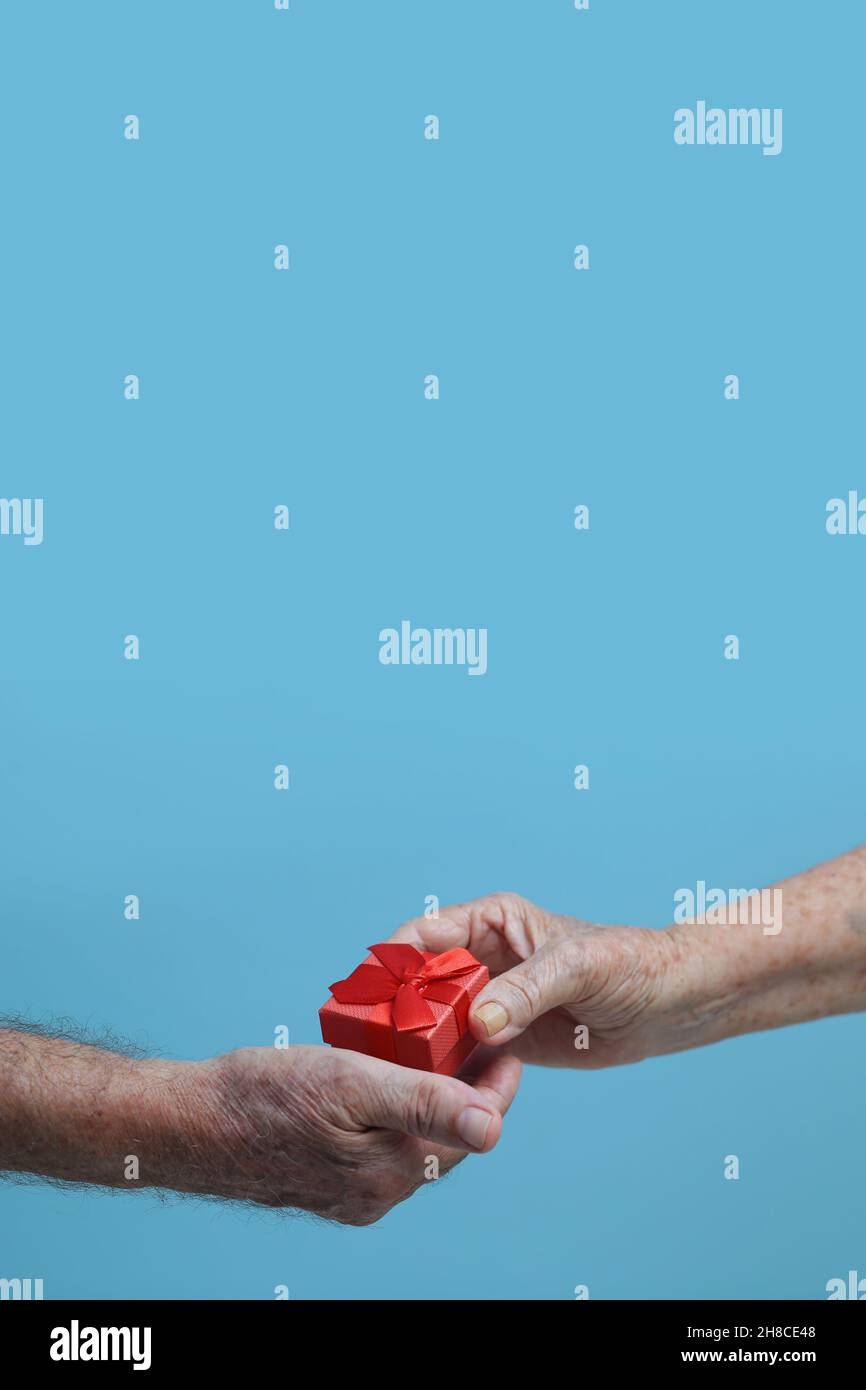 Goiânia, Goias, Brasilien – 29. November 2021: Detail der Hand einer älteren Person, die einer anderen Person mit blauem Hintergrund ein Geschenk anbietet. Stockfoto